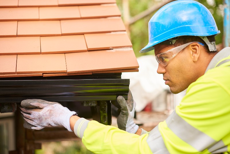 Man installing gutter on the side of a house by Bryan Exteriors