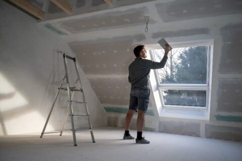 Man finishing the drywall in an attic by Bryan Exteriors